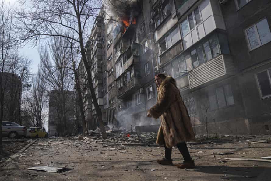 A woman walks past a burning apartment building after shelling.
