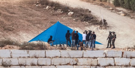 Israeli soldiers watch Israeli settlers setting up a tent just outside the entrance of a besieged Palestinian family home in the village of Qusra