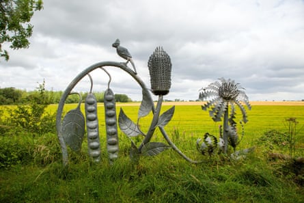 A steel sculpture of a bird sitting on a loop with flowers, leaves and bean pods.