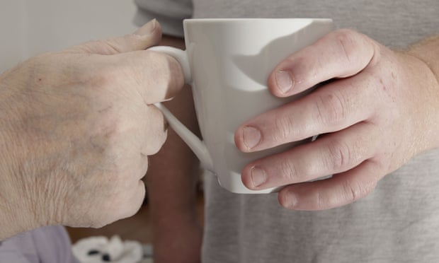 A carer hands a cup to an elderly man