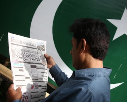 A man reading a newspaper in front of a Pakistan flag