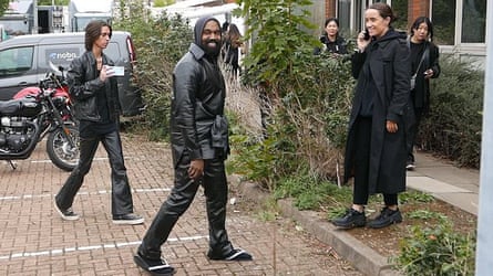 a with a phone in his hand records another man walking and smiling as three other people stand near them