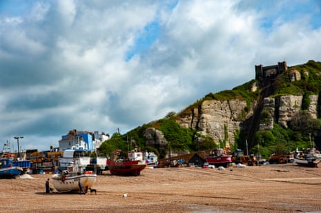 Fishing boats on a shingle beach backed by grass-topped cliffs on a sunny day