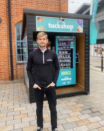 Jacob stands in front of a blue Tuckshop vending machine.