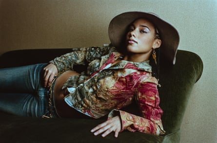 Keys, wearing a wide brimmed hat, a short, colourful jacket and jeans, reclines on a sofa