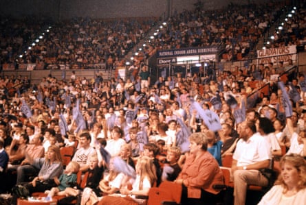 Lots of people sitting in an arena, in the audience for the original version of the Gladiators TV series, in the 1990s