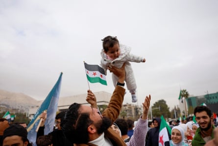 A man holds up a baby as people wave Syria flags