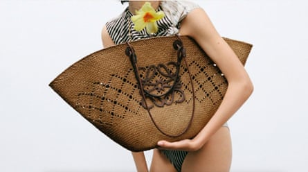 Large flat-sided raffia bag with large Loewe logo is held in a model’s arms