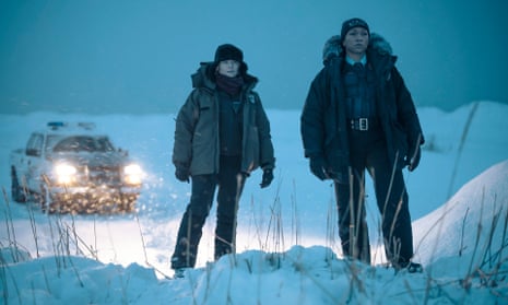 Jodie Foster (left) and Kali Reis as Danvers standing in a gloomy snow-covered landscape in front of a police car with its lights on.