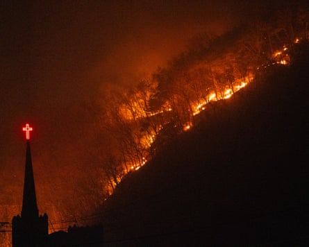 Church spire with cross with wildfire roaring through trees at night