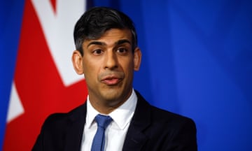 Rishi Sunak stands in front of a blue backdrop with a union flag to the left