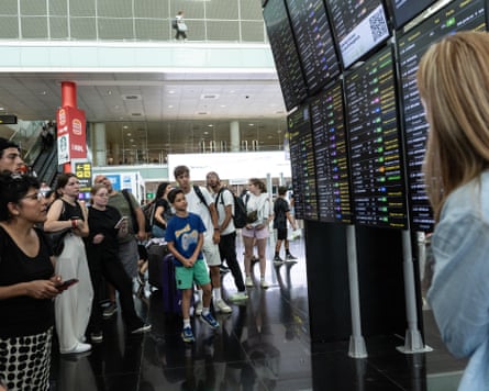 Passengers look at a screen displaying delayed flights at Barcelona airport