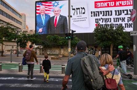 Pedestrians in Tel Aviv cross beneath a billboard showing Trump and Netanyahu