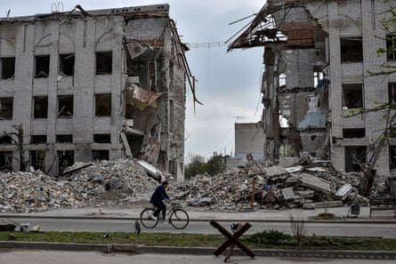 A woman riding a bicycle in front of a building destroyed by a Russian airstrike