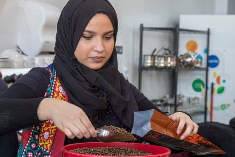 A woman in a black headscarf scoops coffee beans into a bucket at Qahwah House