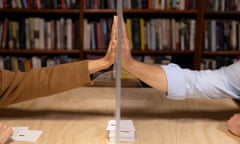Hands reach across a table to touch a clear screen above a stack of printed cards