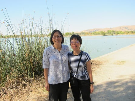 Two women standing side by side, smiling, a b each behind them