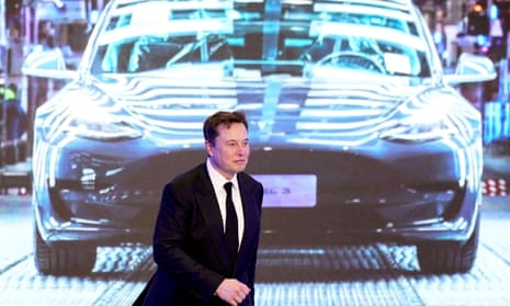 Elon Musk walks next to a screen showing an image of a Tesla Model 3 car during a ceremony in Shanghai, China in 2020