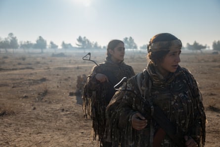 Two female Kurdish soldiers looking to the right of the image with scrubland in the background