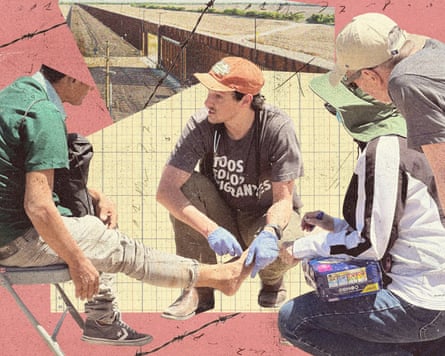 A person examining an injured foot while two others sit beside him, with the border wall in the background