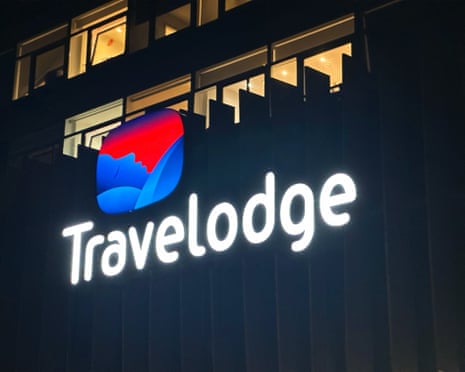 A lit-up Travelodge sign at night.