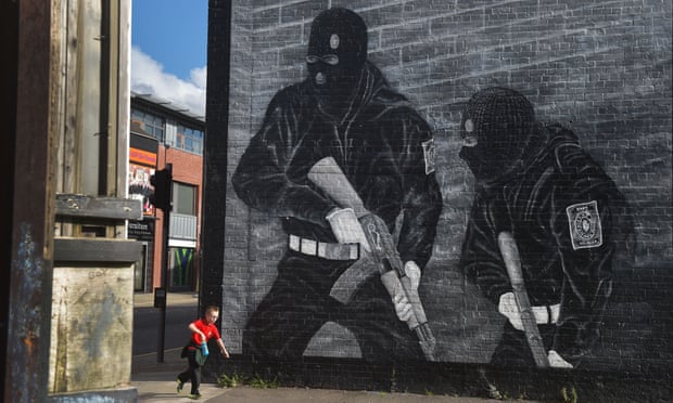 A boy runs past a mural of loyalist paramilitaries in Belfast
