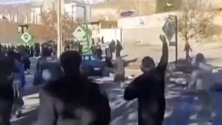 Blurred image of people clustered in a street; one man in front of the camera is raising his fist.