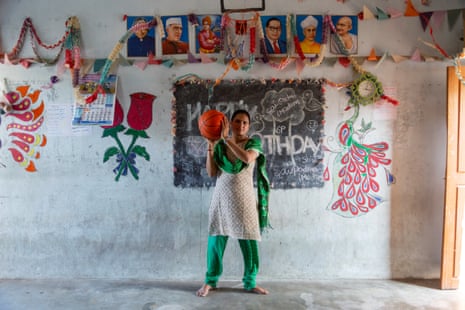 Pandranki holding a basket ball, standing in front of a wall decorated with flower and bird murals and a blackboard with happy birthday written on it