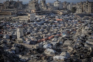 Aerial view of tents crammed together with damaged blocks of flats in background