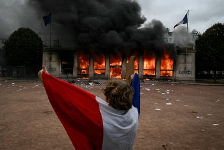 A protester wrapped in a French national flag stands in front of Lyon’s burning tourism office.