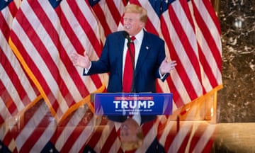 Trump in suit and tie speaks in front of multiple American flags