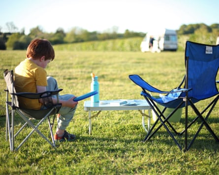 A child sits on a camping chair beside an empty chair in a field