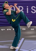 B-Girl Raygun, in a baseball cap and T-shirt and loose leggings labelled “Australia”, breakdances by lifting her right leg, bending backwards and putting her arms in a praying mantis position