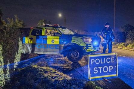 An armed police officer stands by a police car at a road block close to RAF Fairford