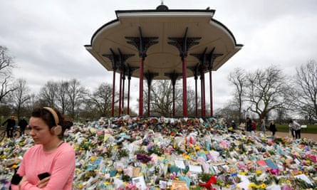 A bandstand surrounded by bunches of flowers with a woman walking by.