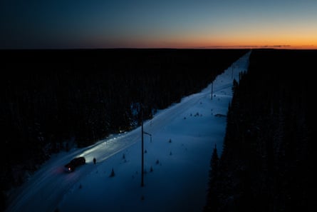 A truck drives down a winter road in semi-darkness; the sun is seen as a thin orange stripe on the horizon.