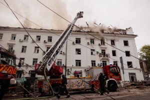 A mechanical ladder with platform extends from a fire engine next to a white residential block as smoke rises above the roof
