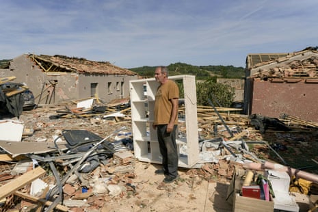 A man stands among the rubble of a damaged house.