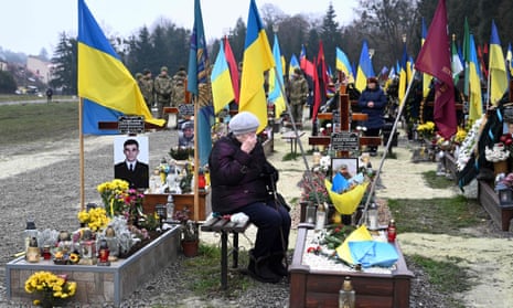 An elderly woman grieves next to the grave of a Ukrainian soldier.