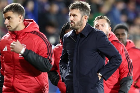 Michael Carrick walks off the pitch, hands in his pockets, with players in red jackets behind him