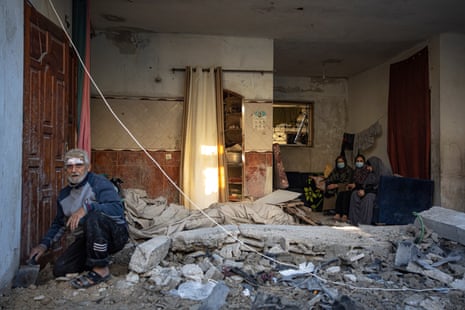 A man inspects his home as women sit further back from the rubble