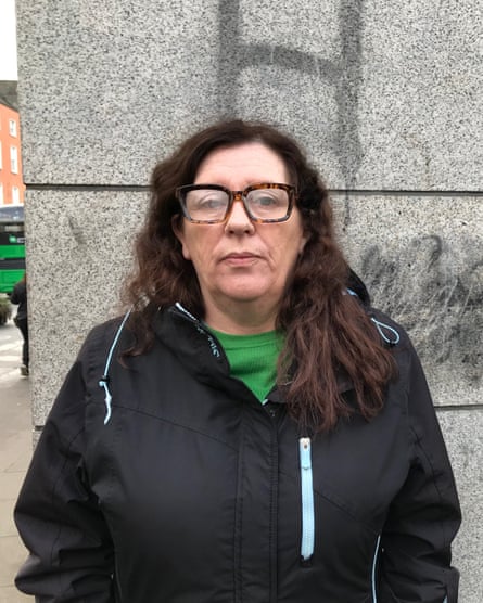 Siobhán Kearney – in a hooded coat, T-shirt and glasses – stands against a concrete wall