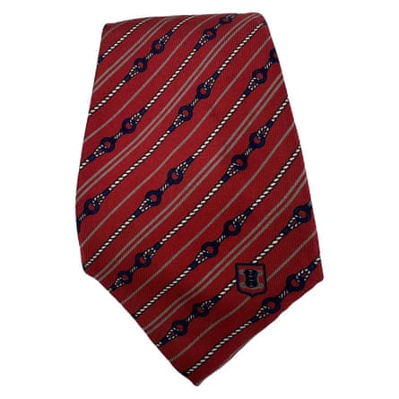 A red Celine tie with Triomphe logo and horse bit pattern.
