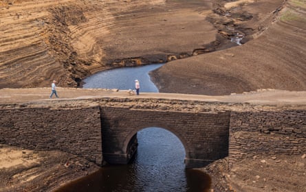 People walk over a Viking-era packhorse bridge in a dried-up reservoir