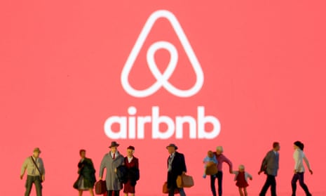 Small toy figures are seen in front of diplayed Airbnb logo