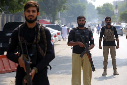 Three armed security officials stand on guard in the middle of a road