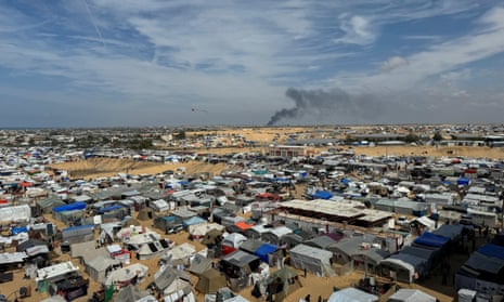 Smoke from Israel’s military operation is seen rising in the distance in this view from 14 March of one of the makeshift tent camps that Palestinians from Gaza are being forced to live in.