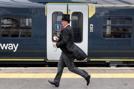 A man in a top hat runs with a coffee cup and a bottle of water to catch a train at Waterloo Station to travel to Royal Ascot.