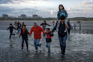 People hold hands as they walk fully clothed into the sea to board a small boat