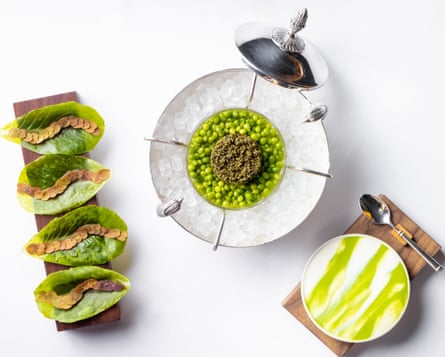 Four lettuce leaves on a platter, next to a plate of peas with a bowl of cream with a green drizzle on the bottom right, all fancily plated